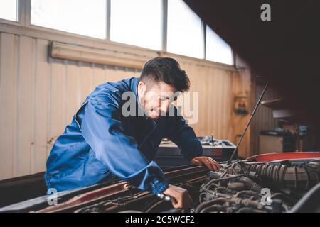 Un mécanicien automobile masculin en uniforme bleu est en train de réparer une voiture Banque D'Images