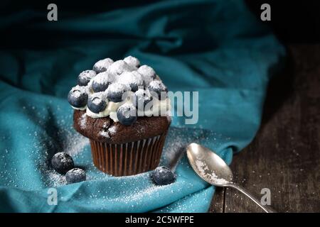 Muffin au chocolat à la crème douce et aux bleuets frais en poudre de sucre, fond rustique Banque D'Images