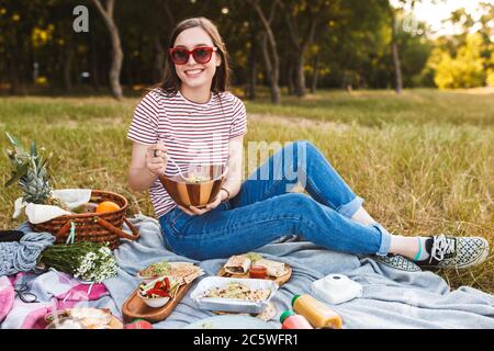 Belle fille dans des lunettes de soleil contenant un bol avec salade assis Banque D'Images