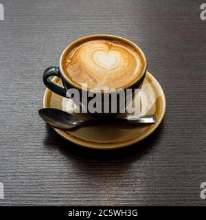 Une tasse de café crémeux avec un motif de coeur et une cuillère sur une soucoupe Banque D'Images