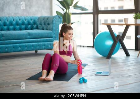 Jolie fille avec une bouteille d'eau regarder des sports vidéo tutoriel sur le tapis de yoga à la maison Banque D'Images