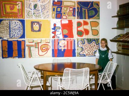 Jeune fille de six ans debout fièrement par son résumé Tableaux d'art exposés sur un mur de salle à manger aux États-Unis dans les années 1960 Banque D'Images