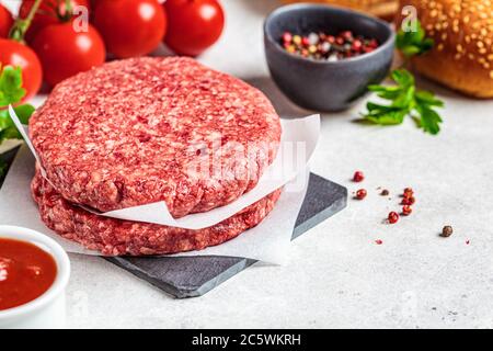 Patties de hamburger crues sur le tableau, fond blanc. Banque D'Images