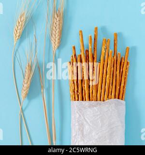 Bâtonnets de blé salés, cuits au four dans un sac en papier écologique blanc avec des épillets de blé sur fond bleu Banque D'Images