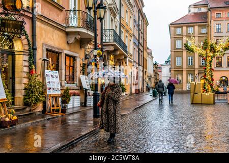 Varsovie, Pologne - 22 décembre 2019 : une femme touristique qui tient des achats de parapluie sur la place du marché de la vieille ville de Varsovie en soirée sous la pluie pendant l'hiver Banque D'Images