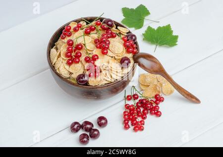 Flocons de maïs frais, raisins de Corinthe et cerises dans un bol rond sur fond de bois. Banque D'Images