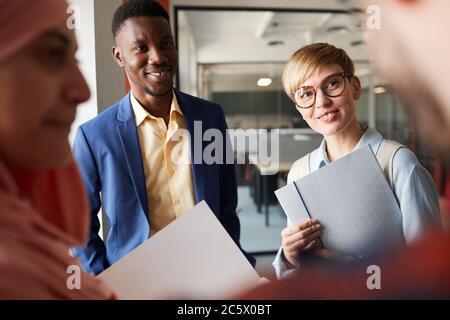 Gros plan sur les discussions multiethniques d'une équipe d'affaires debout au bureau, se concentrant sur le sourire des femmes de race blanche et des jeunes hommes d'affaires afro-américains Banque D'Images