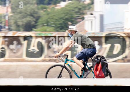 Belgrade, Serbie - 4 juillet 2020 : un jeune homme beau portant un chapeau de paille et un masque chirurgical à vélo sur le pont de rue de la ville Banque D'Images