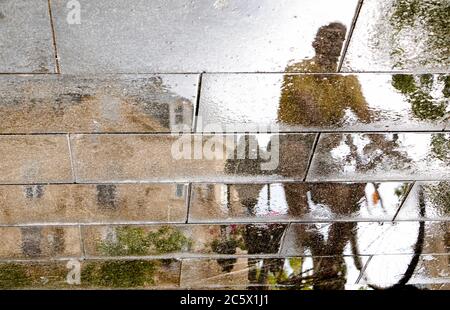 Silhouette d'ombre floue et réflexion d'un homme qui fait du vélo sur une flaque de rue humide dans la zone piétonne de la ville, par une journée d'été pluvieuse et ensoleillée, basse A. Banque D'Images