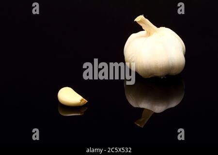 Bulbe d'ail allium sativum et une gousse isolée sur verre noir avec réflexion Banque D'Images