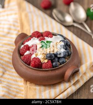 Granola au yogourt blanc aux framboises et aux bleuets dans un bol en céramique sur une serviette en papier. Banque D'Images