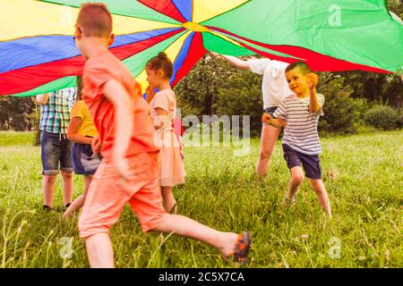 Enfants qui jouent en cercle sous un parachute coloré Banque D'Images