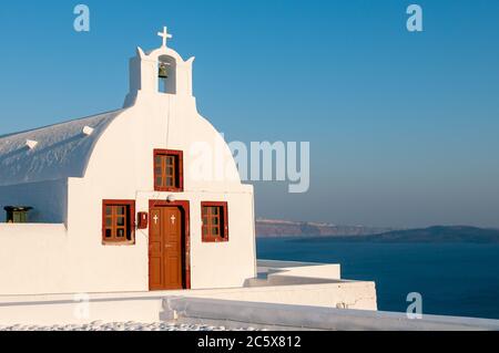 Petite église blanche traditionnelle au coucher du soleil village d'Oia en mer Égée sur l'île grecque de Santorini en Grèce Banque D'Images