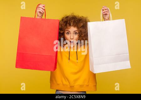 Portrait de shopper choqué, fille à poil dur émerveillé dans des sacs à capuche soulevant des sacs d'achats avec zone vide, copier l'espace sur les paquets pour le texte publicitaire. Dans Banque D'Images