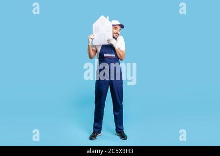 Homme de main plein de gai, ouvrier du bâtiment en uniforme peeking hors de la maison de papier et souriant à l'appareil photo. Un homme de la Motte qui offre de l'aide pour la mutation, hom Banque D'Images