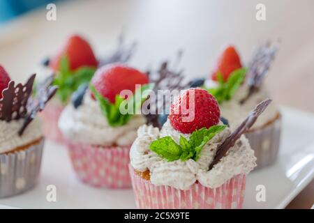 Magnifique groupe coloré de petits gâteaux décorés de crème fouettée blanche, de fraises, de bleuets, de chocolat et de menthe sur une table en bois. Banque D'Images