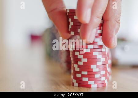 Sélection de l'accent sur des piles de jetons de poker en plastique rouge sur une table en bois, mouvement des jetons de ramassage à la main et flou artistique sur fond bleu et vert. Banque D'Images