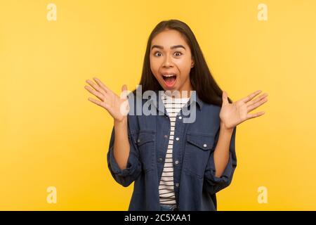 Oh mon dieu, wow! Portrait de la jeune fille excitée dans un maillot en denim debout avec les mains levées et criant dans l'étonnement, surpris par des suces incroyables Banque D'Images