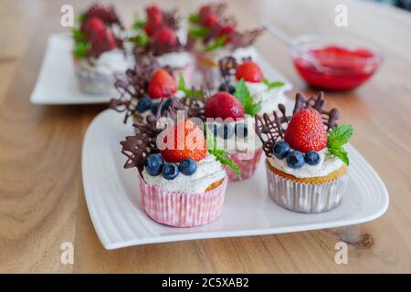 Magnifique groupe coloré de petits gâteaux décorés de crème fouettée blanche, de fraises, de bleuets, de chocolat et de menthe sur une table en bois. Banque D'Images