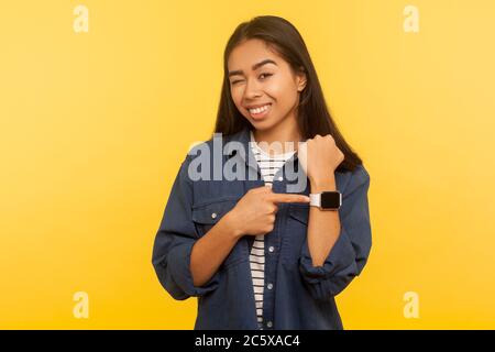 Souvenez-vous de l'heure ! Portrait de fille gaie en denim montre-bracelet pointant et wencant avec un jeu, montrant l'heure de réunion convenue, Happy minutes. ind Banque D'Images