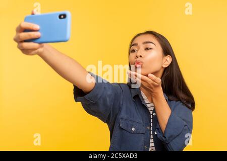 Portrait de belle fille élégante belle en denim shirt prenant selfie ou parlant sur appel vidéo et envoyant un baiser d'air, agréable communication en ligne vi Banque D'Images
