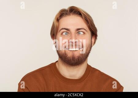 Gros plan portrait de l'homme idiot, muet barbu regardant en travers des yeux avec le sourire stupide, se tromper autour, faire le visage stupide, l'expression comique sans cerveau. ind Banque D'Images