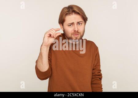 Quelques pouces, centimètre. Portrait de drôle malheureux barbu homme regardant déçu et montrant un petit geste, petite quantité ou bas signe d'échelle Banque D'Images