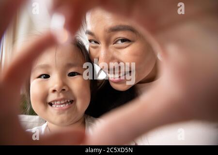 Petite fille asiatique faisant le geste du coeur avec maman souriante. Banque D'Images