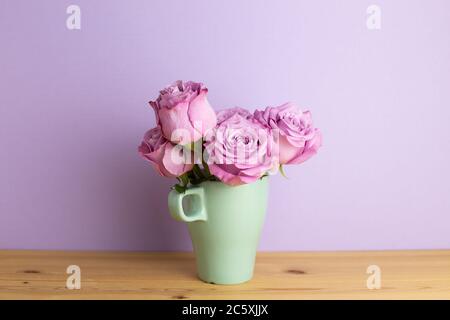 Fleurs roses violettes dans une tasse sur une table en bois avec fond violet. Espace de copie Banque D'Images