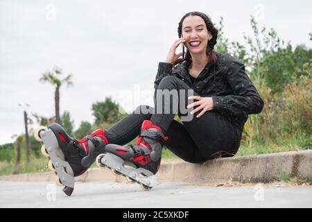 Une femme heureuse en train de faire une pause pour le patinage à roulettes, assise dans la rue et utilisant un téléphone portable. Jolie, Urban Girl parlant au téléphone, portant des patins à roulettes. Fille moderne dans la ville . Photo de haute qualité Banque D'Images