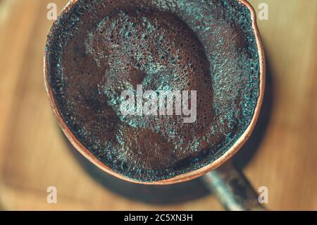 Café naturel avec mousse épaisse, brassé dans une cève de cuivre de la manière classique, sur un fond de bois, photo macro. Banque D'Images