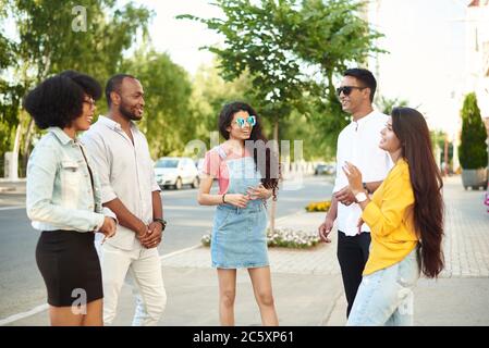 Concept de « Bonding Outdoors » pour les jeunes de groupe divers. Communication des amis de différentes races sur le fond de la ville et de la rue. Banque D'Images