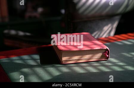 Sainte bible sur le dessus de la table en bois rouge et en cuir vert. Jeu léger formant des motifs de lignes et des ombres. Banque D'Images