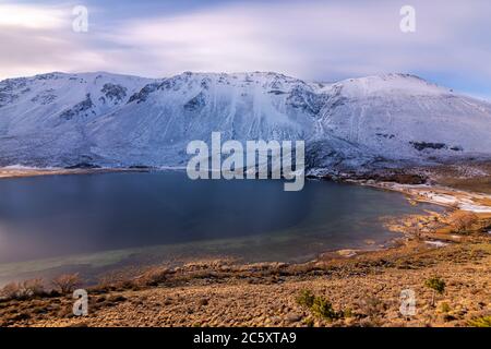 Photo d'un lac de montagne en exposition prolongée contre des montagnes enneigées au coucher du soleil en hiver, Esquel, Patagonie, Argentine Banque D'Images