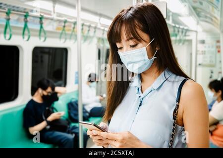 Jeune femme asiatique passager portant un masque chirurgical et utilisant un téléphone portable dans le métro Banque D'Images