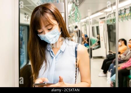 Jeune femme asiatique passager portant un masque chirurgical et utilisant un téléphone portable dans le métro Banque D'Images