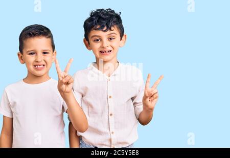 Couple de petits frères ensemble portant des vêtements décontractés souriant avec le visage heureux qui se vante à la caméra faisant signe de victoire. Numéro deux. Banque D'Images