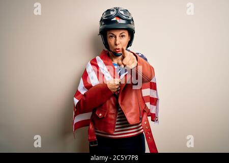 Femme motocycliste d'âge moyen portant un casque de moto et drapeau des états-unis pointant avec le doigt vers la caméra et vers vous, signe de main, positif et Banque D'Images