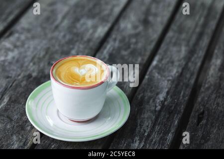 Tasse de cappuccino crémeux frais avec art du lait en coeur sur mousse. Arrière-plan de table en bois noir foncé avec surface vieillie. Espace vide. Banque D'Images