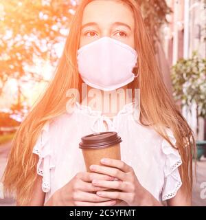 Fille tenant une tasse de café en papier. Masque de mise à zéro des déchets. Nouvelle normale Banque D'Images