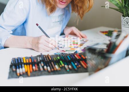 Rognez la photo de la jeune femme avec un illustrateur de cheveux rouges, l'artiste dessine à un bureau à la maison Banque D'Images