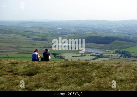 Un couple assis et appréciant la vue des réservoirs de mousse noire du sommet de Pendle Hill sur le sentier de Pendle Way de l'orge, Lancashire, Royaume-Uni. Banque D'Images