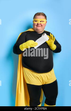 jeune caucasien frissant gros homme conçu quelque part, il regarde à côté et tient le papier toilette dans les mains, portant le costume jaune et des gants de protection. Banque D'Images