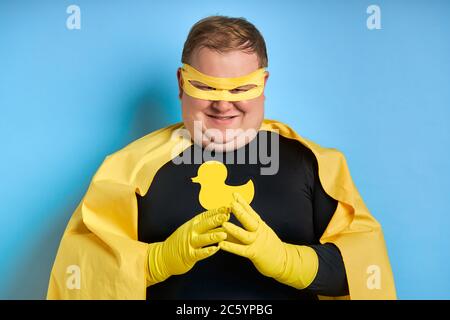 jeune caucasien frissant gros homme conçu quelque part, il regarde la caméra, portant le costume jaune et des gants protecteurs. isolé fond bleu Banque D'Images