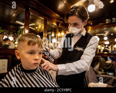 Stephen Hill coupe les cheveux de Ruairi Gargan, six ans, à Cambridge Barbershop sur Lisburn Road de Belfast, qui a ouvert à 00 h 01, alors que les coiffeurs et salons de beauté rouvrent en Irlande du Nord, une partie de la dernière mesure visant à atténuer les restrictions du coronavirus. Banque D'Images