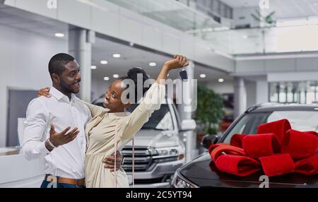 beau homme à la peau sombre plaît sa femme dans la concession, il donne la voiture comme une femme et un homme heureux présent dans l'amour Banque D'Images