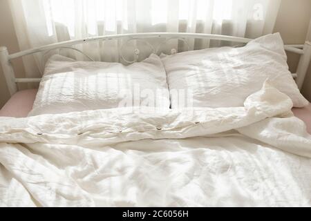 Belle lumière du matin dans la chambre. Literie blanche aux couleurs pastel. Linge de lit bio tendance en lin naturel. Intérieur confortable. Banque D'Images