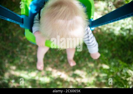 Un petit garçon qui s'amuse à jouer sur une balançoire sous un arbre dans un jardin Banque D'Images