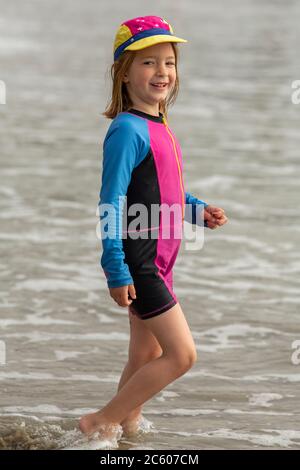 Jeune fille de six ans, dans un maillot de bain lumineux courant et jouant sur une plage de sable