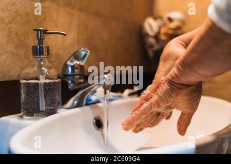 Personne se lavant les mains dans une salle de bains avec un distributeur de savon à côté du robinet avec de l'eau qui sort Banque D'Images